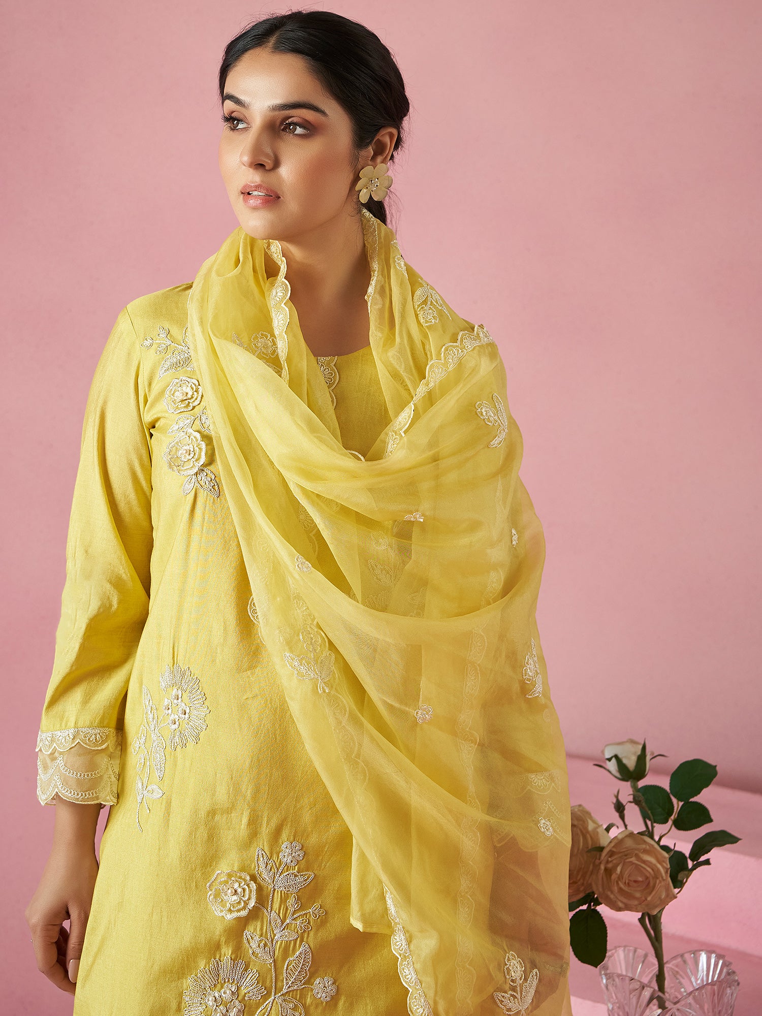 Woman wearing a yellow embroidered outfit with a matching dupatta against a pink background