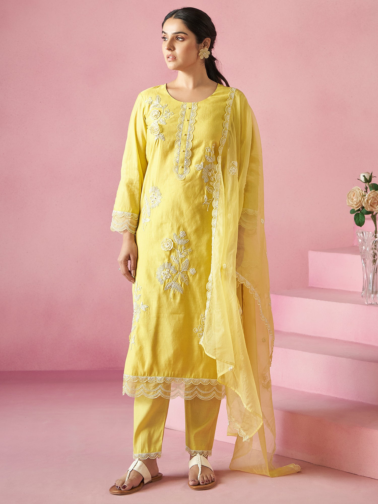 Woman wearing a yellow embroidered outfit with a pink background