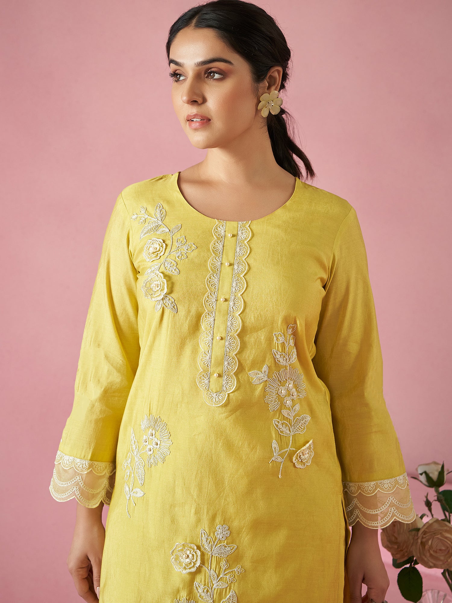 Woman wearing a yellow embroidered dress against a pink background