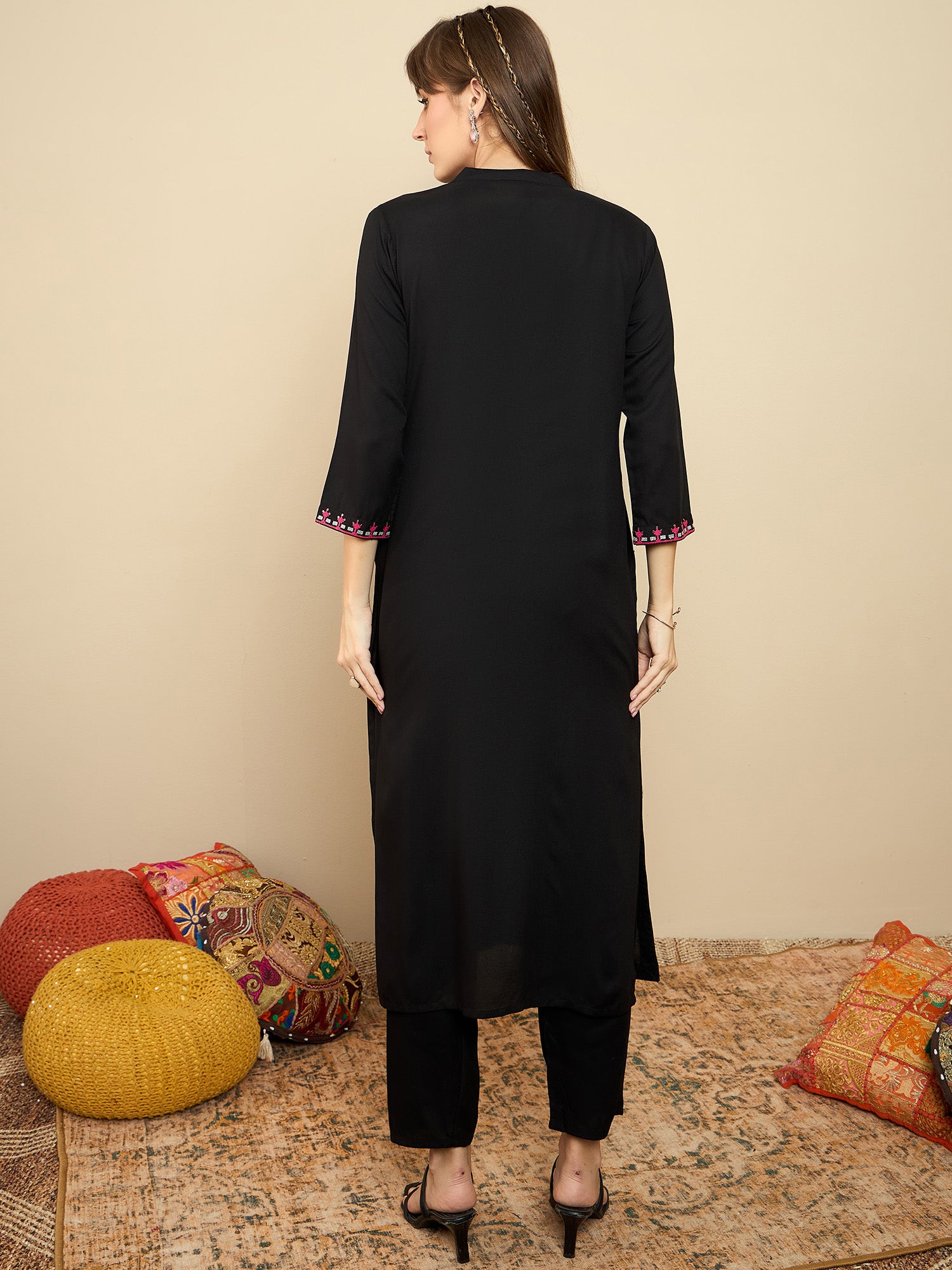 Woman wearing a black kurta with sleeves and pants against a beige wall.