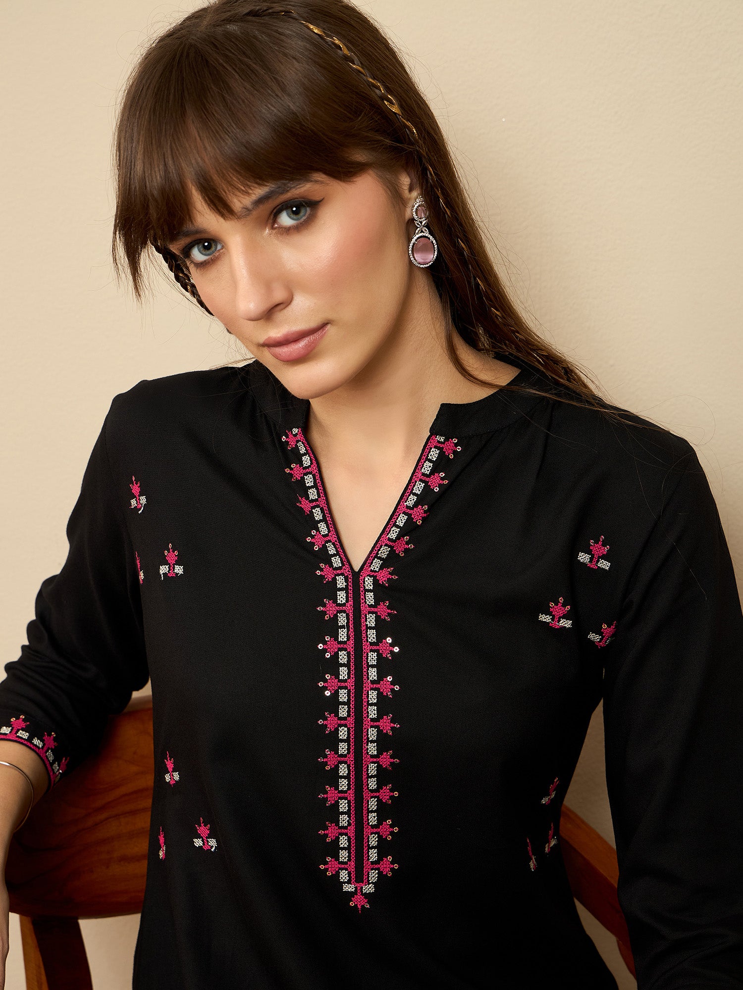 Woman wearing a black top with pink embroidery against a beige background
